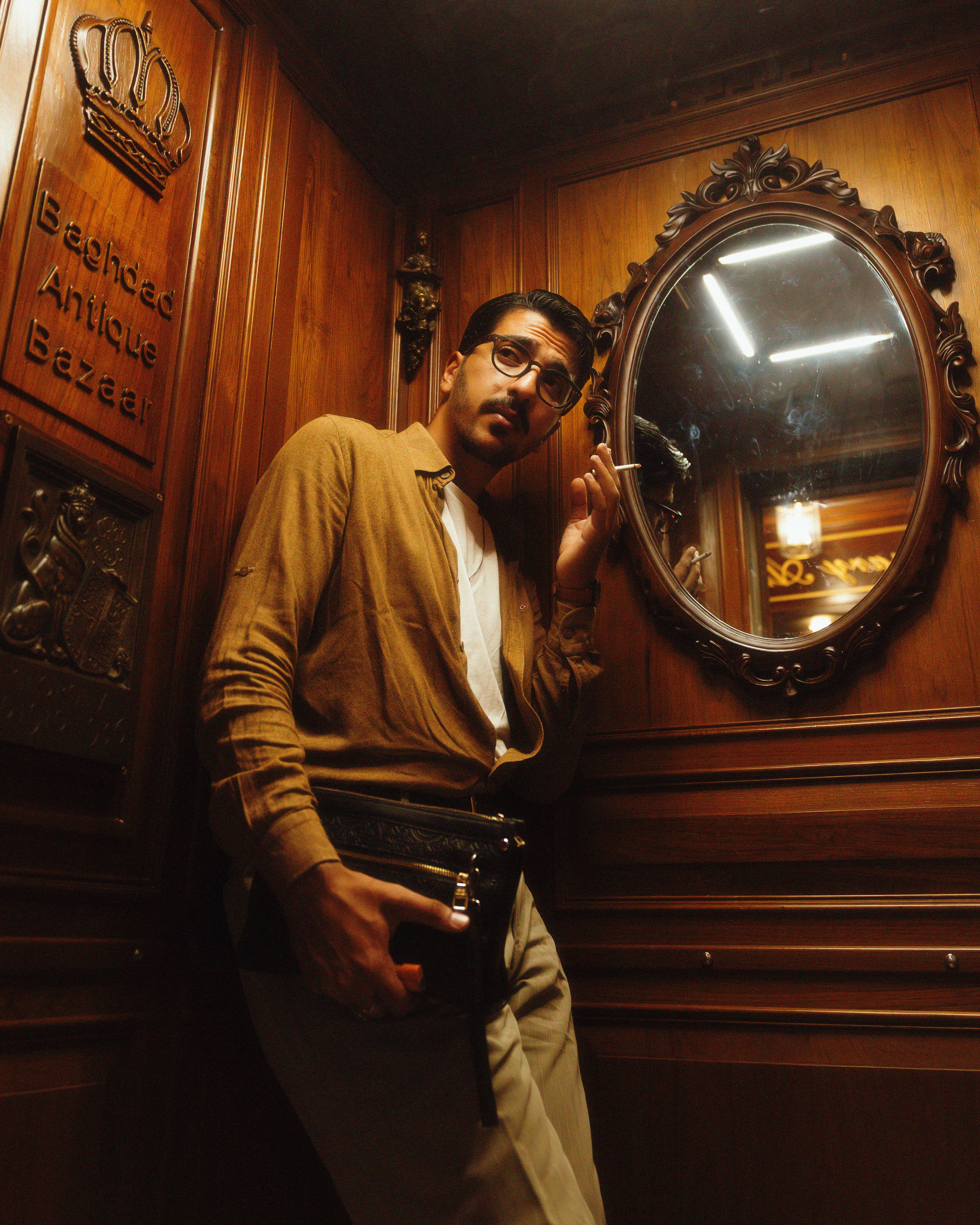 Stylish man posing in vintage setting with ornate mirror and wooden walls.