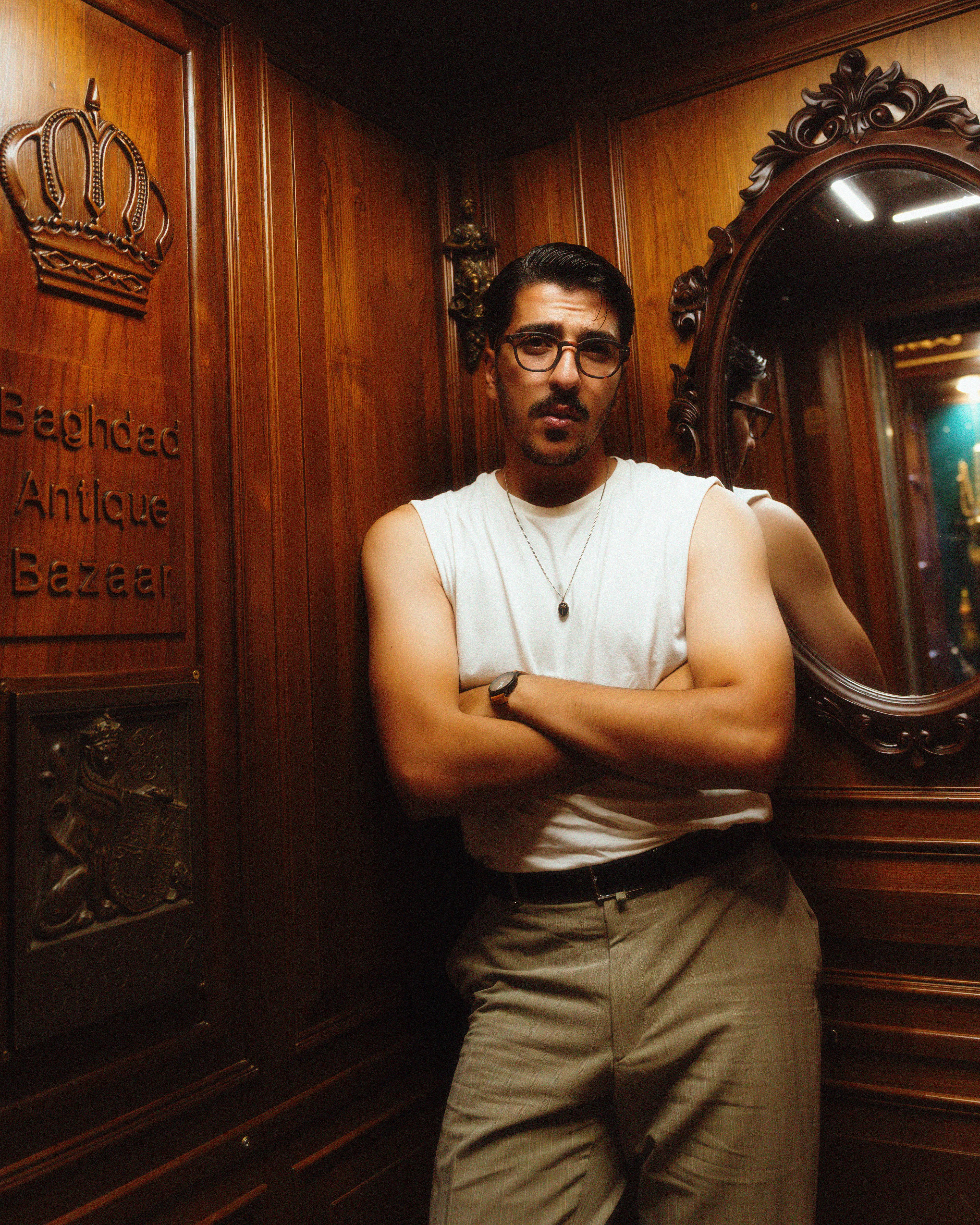 Stylish portrait of a man standing in an antique-themed room with wooden decor and mirrors.