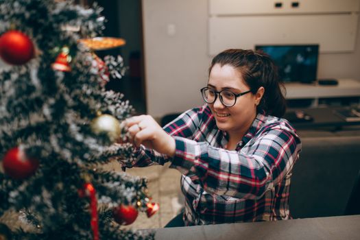 Woman joyfully decorates a Christmas tree indoors, capturing holiday spirit.