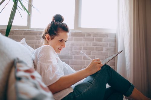 Free A young woman focused on remote work using a tablet in a cozy living room. Stock Photo