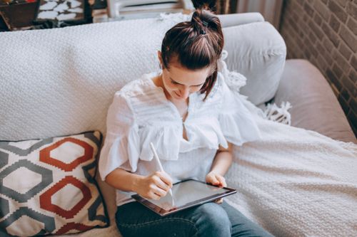 Free Caucasian woman working remotely with tablet in cozy living room setting. Stock Photo