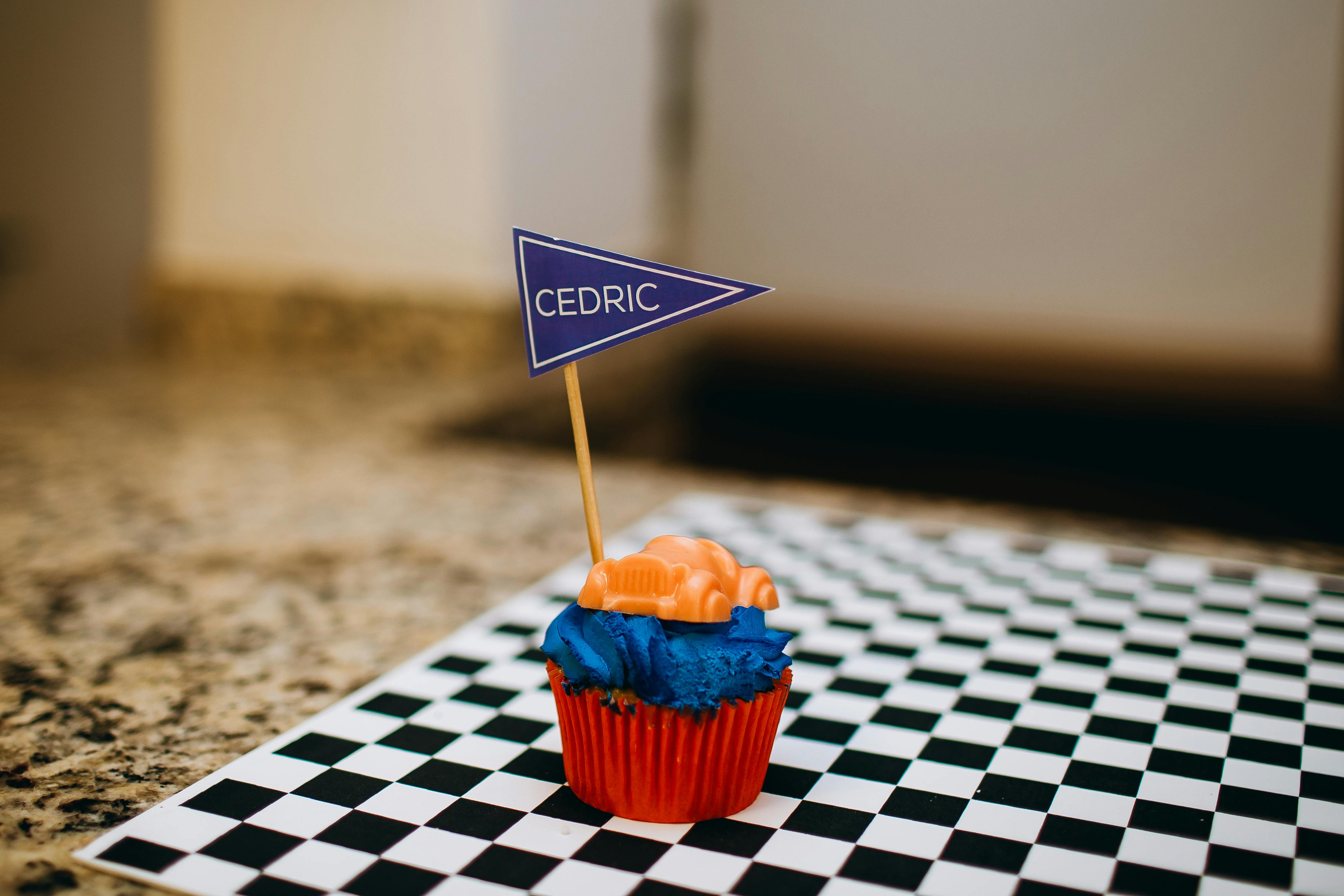Brightly colored cupcake with a name flag on a black and white checkered surface.