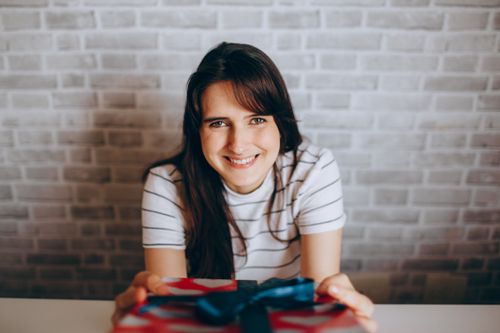 Free A young woman in a striped shirt smiling while holding a wrapped gift box indoors. Stock Photo