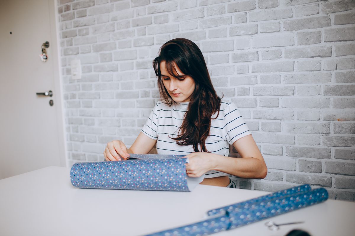 Woman wrapping a gift with blue paper and tape, inspiration for duct tape gift bags