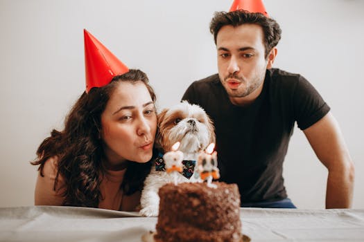 A joyful birthday celebration with a couple and their dog blowing candles on a cake.