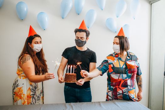 Masked adults celebrating a birthday with cake and sparklers. Safety measures emphasized.