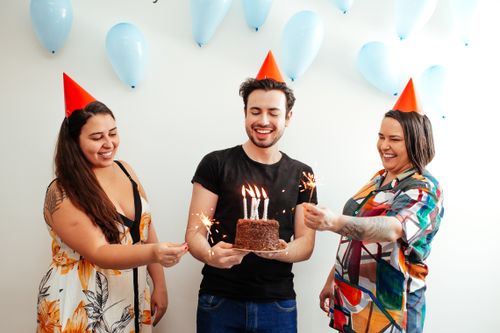 Free Three adults celebrating a birthday with a cake and sparklers indoors. Stock Photo