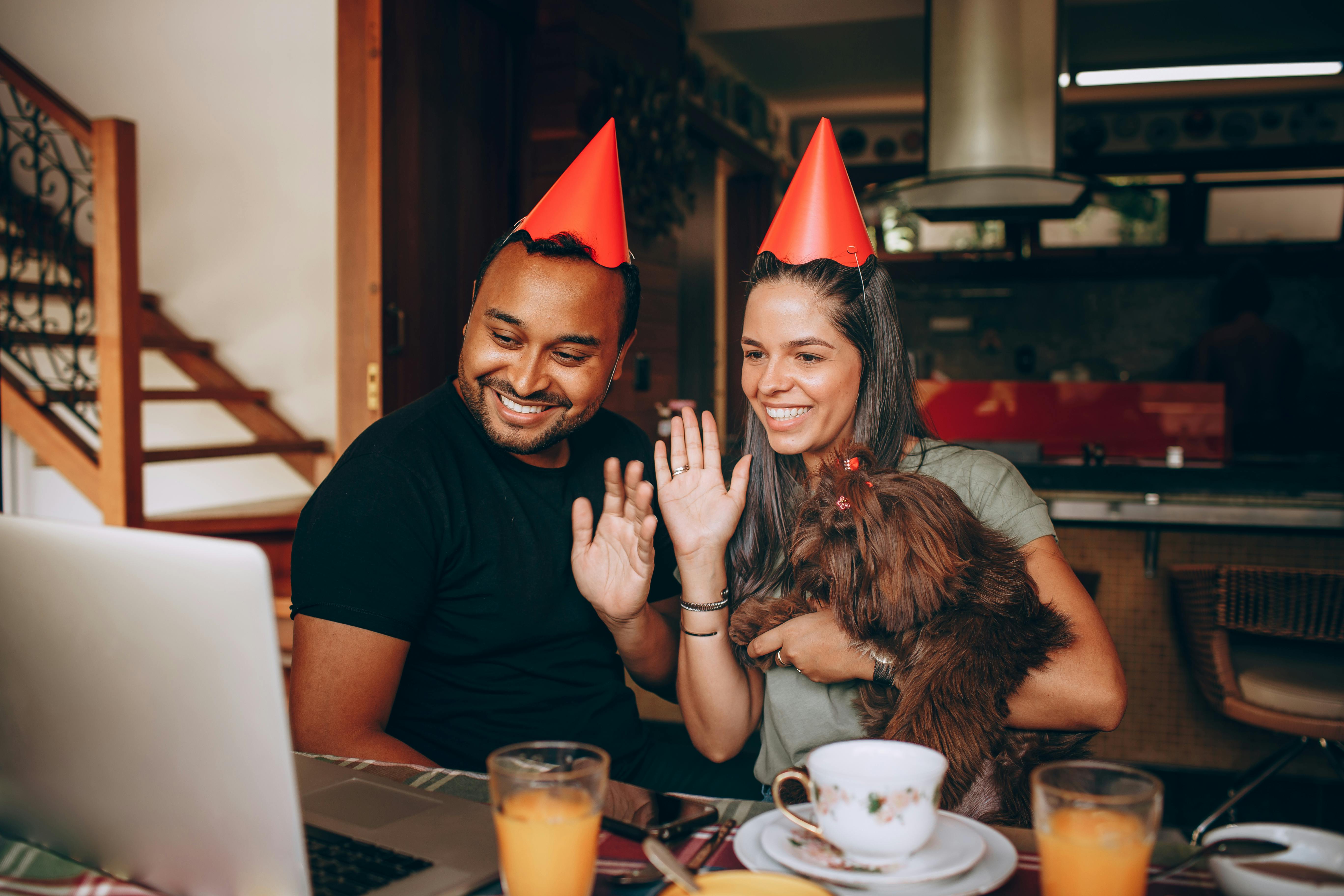 A man and woman wearing party hats and holding a dog