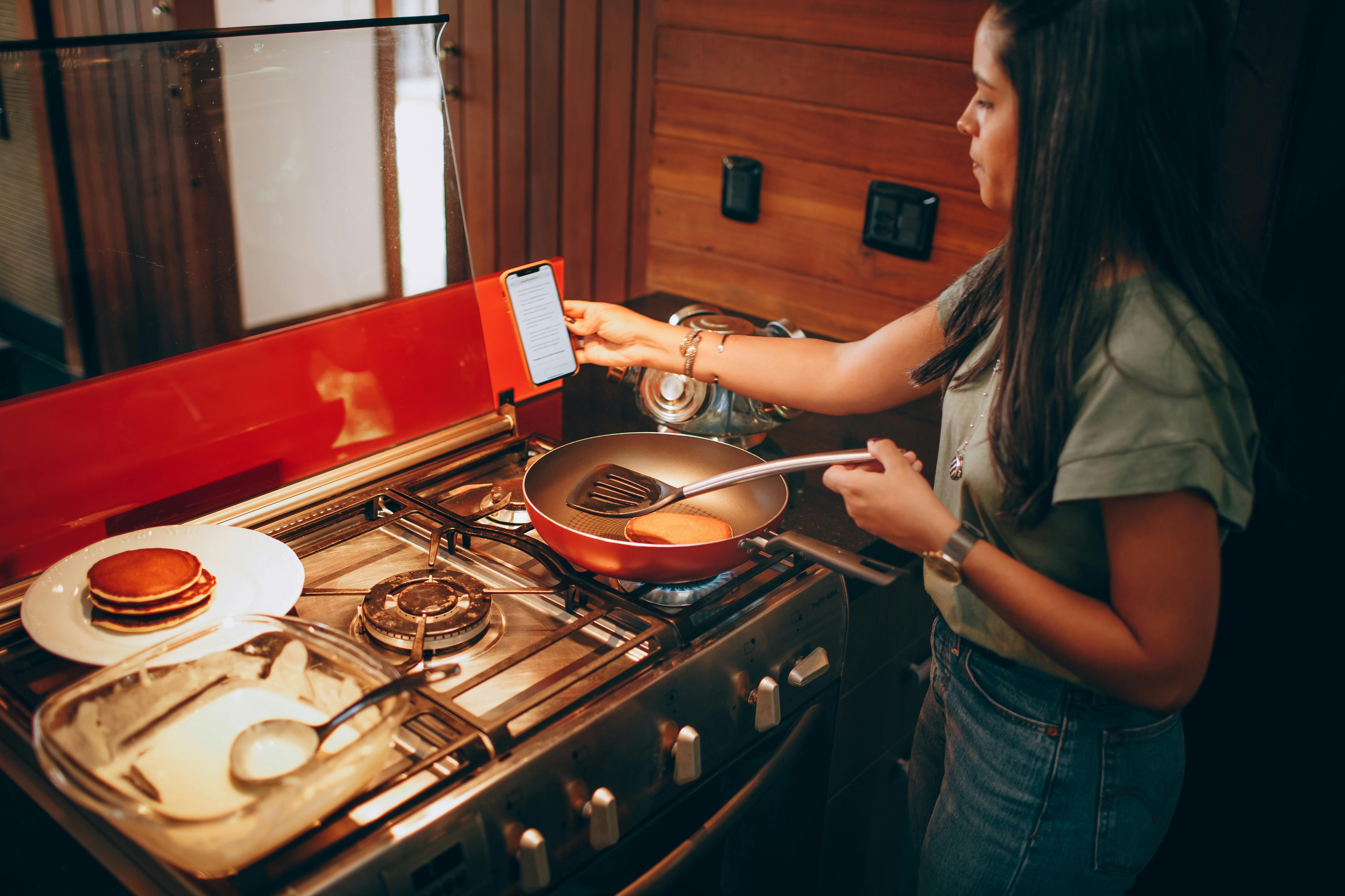 a woman making pancakes and holding her smartphone