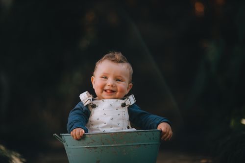 Free Charming baby smiling while sitting in a rustic blue bucket outdoors, embodying joy and innocence. Stock Photo