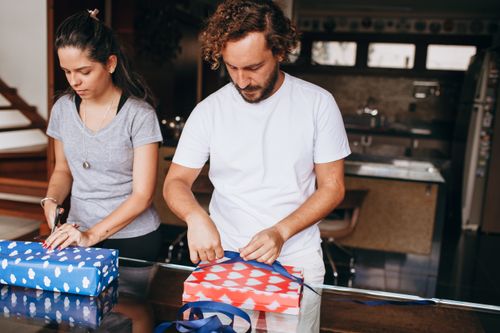 Free A couple wrapping presents in a modern kitchen setting, depicting teamwork and creativity. Stock Photo