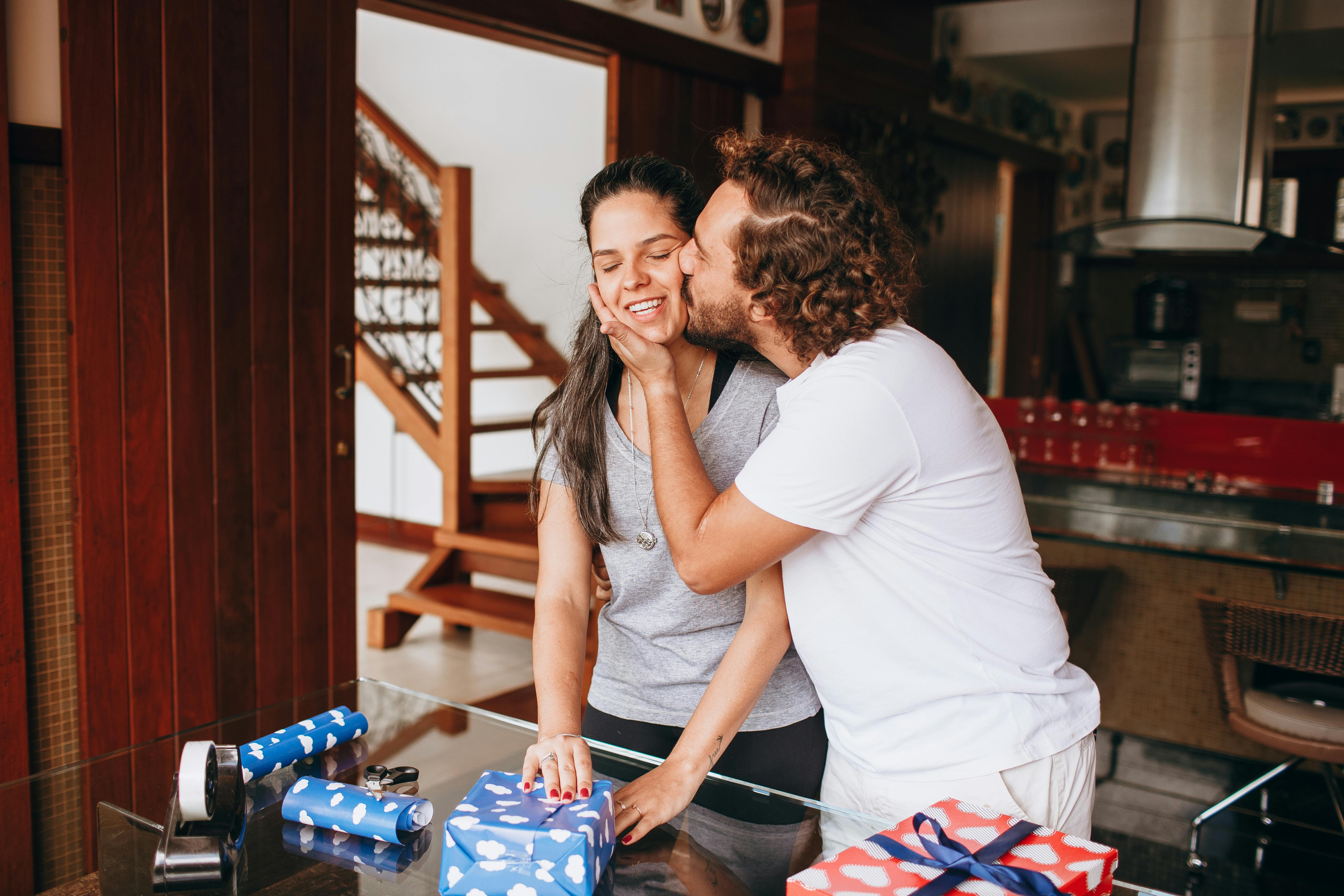 young couple kissing while wrapping christmas presents