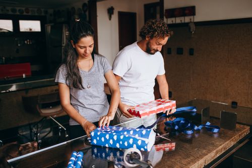 Free A couple enjoys wrapping presents together in a warmly lit, indoor setting. Stock Photo