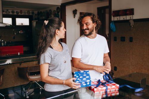 Free A couple sharing a joyful moment exchanging gifts in a cozy modern kitchen setting, fostering love and connection. Stock Photo