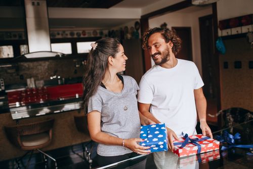 Free Smiling couple exchanging colorful gifts in a stylish kitchen setting, enhancing their joyful bond. Stock Photo
