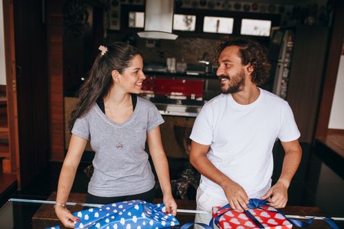 Free Smiling couple wrapping gifts in a cozy home setting, sharing a joyful moment indoors. Stock Photo