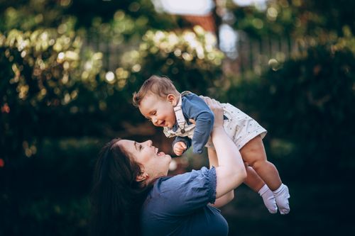 Free A joyful mother lifts her smiling baby outdoors in a summer park, capturing a loving moment. Stock Photo