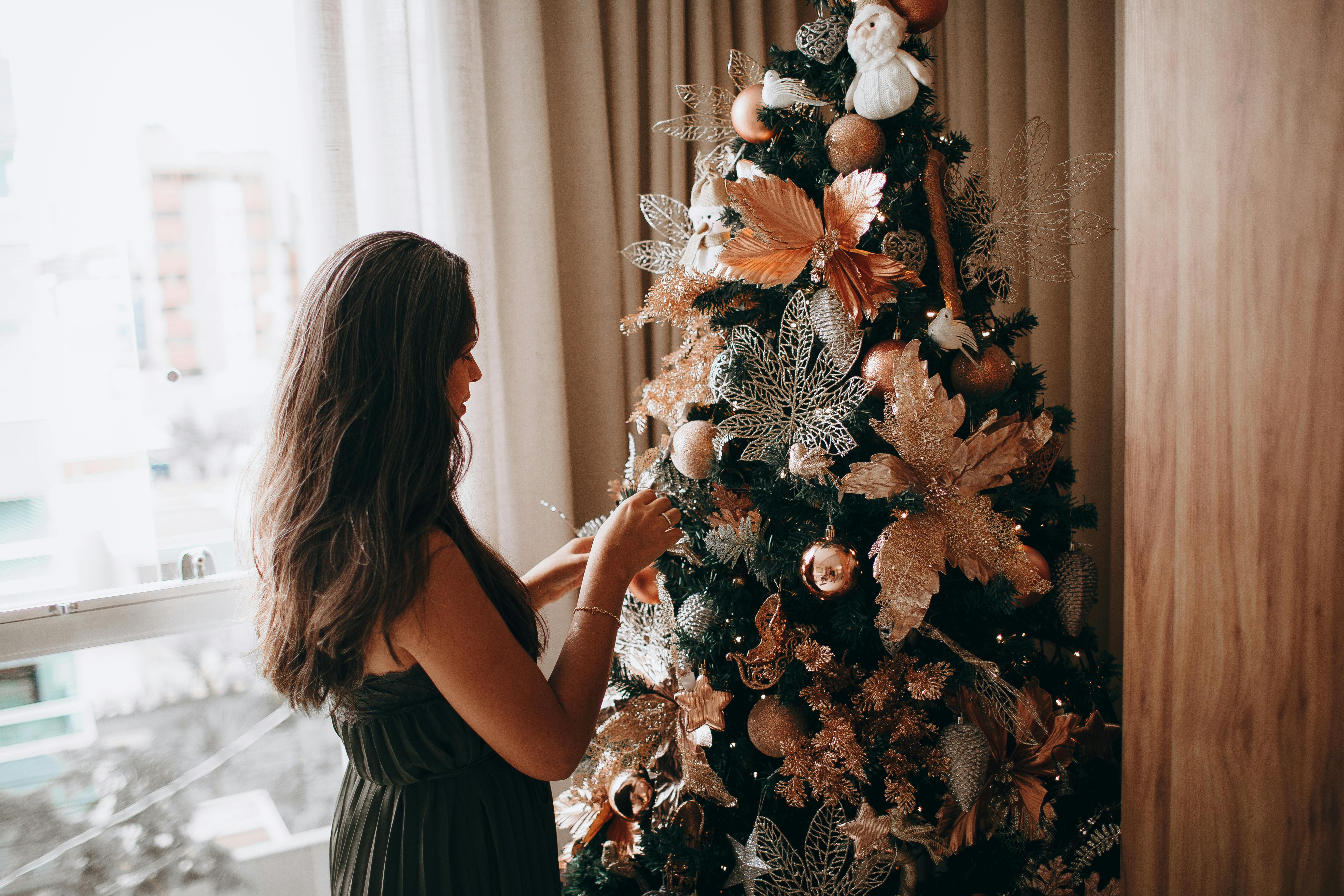 A woman decorates a Christmas tree with golden ornaments in a cozy indoor setting.