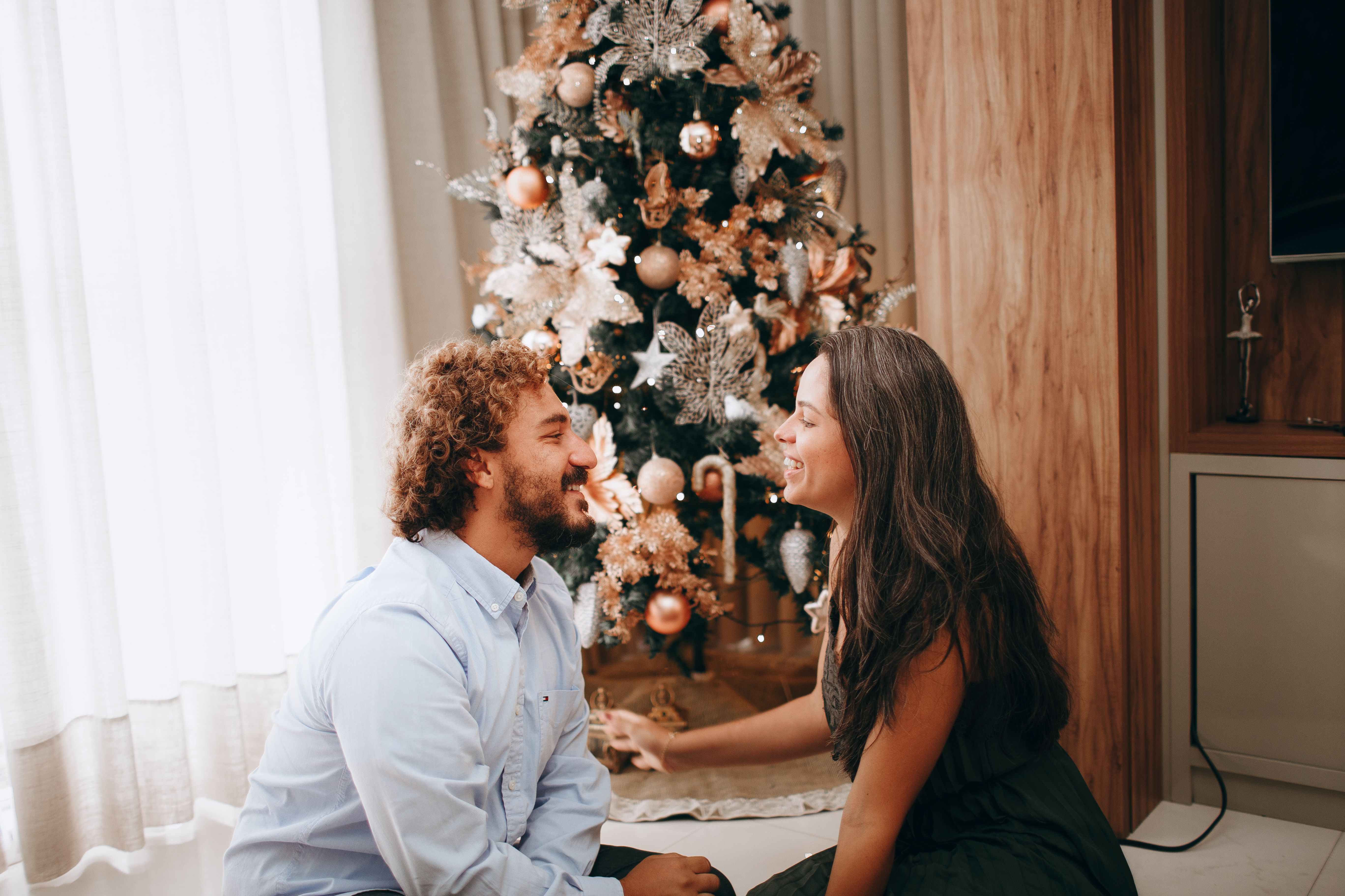 Happy couple sitting by a beautifully decorated Christmas tree, enjoying festive holiday moments.
