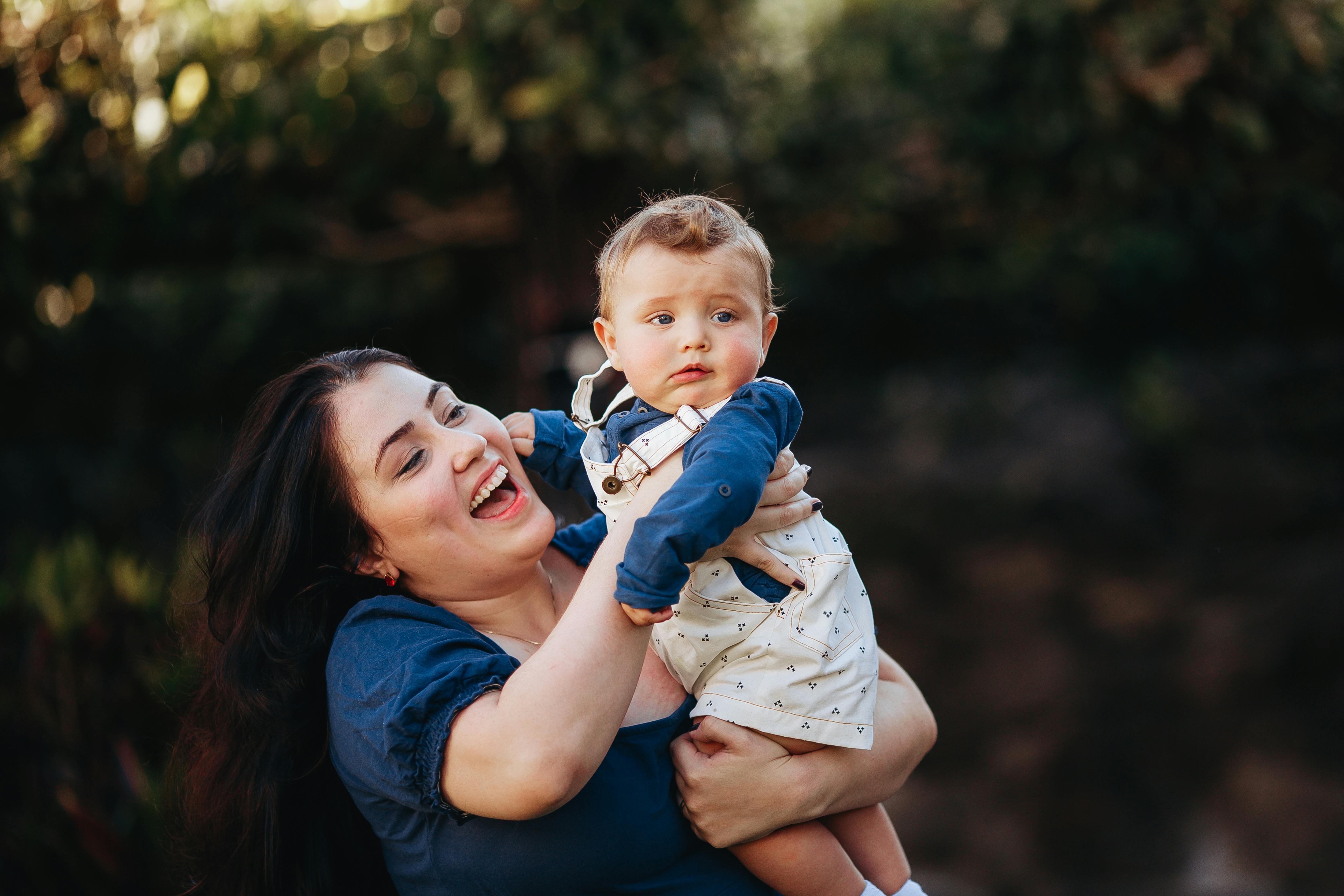 Mother holding baby outdoors, showcasing joy and maternal bond in a natural setting.