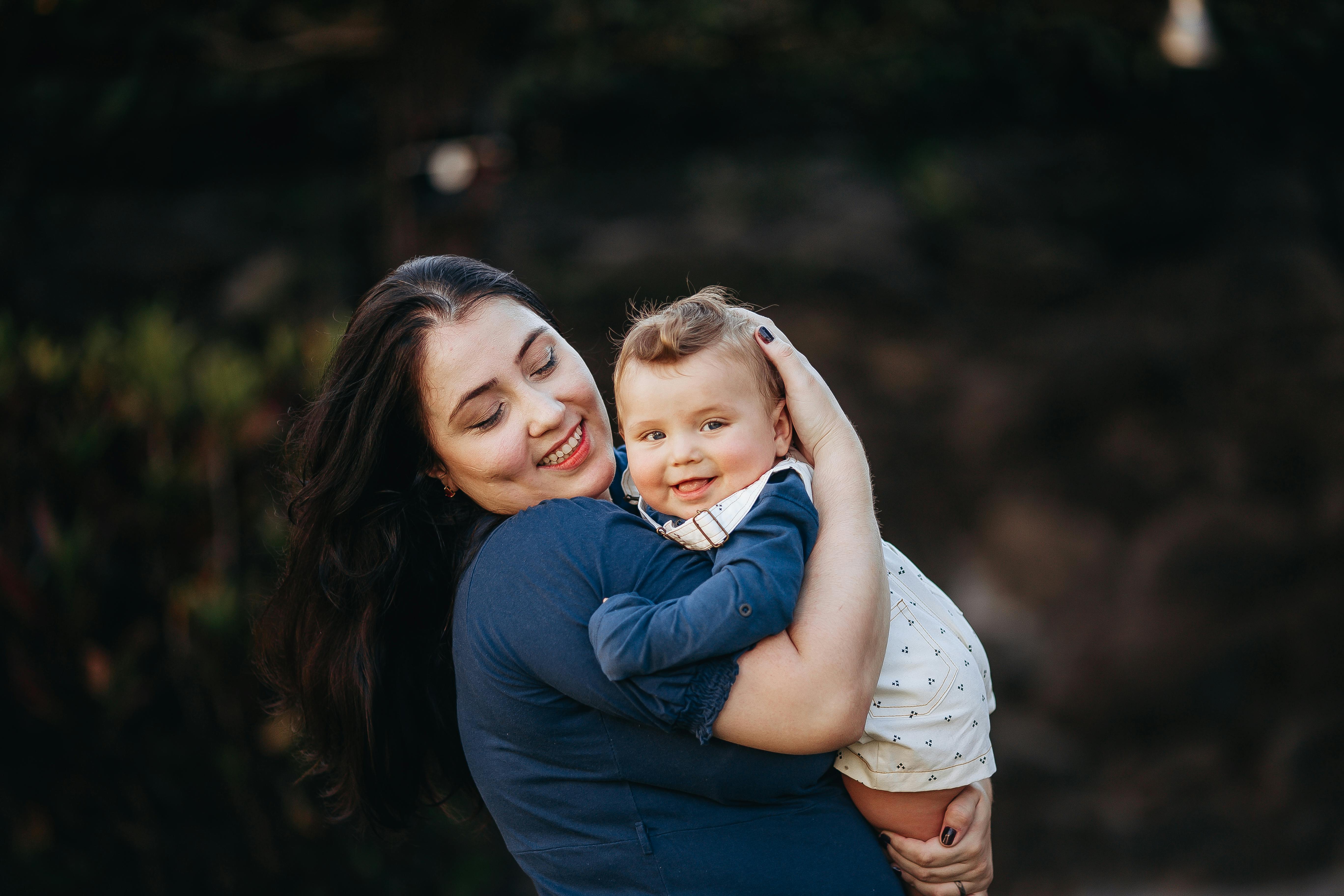 A mother lovingly holding her smiling baby in an outdoor setting with a warm atmosphere.