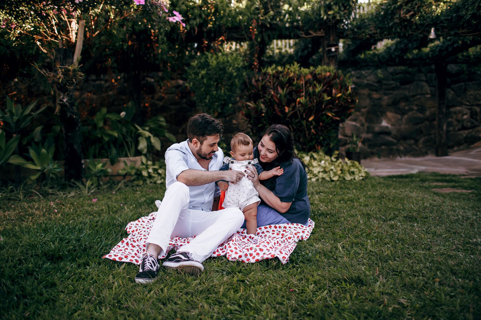 Parents sharing a quiet moment with their baby on a blanket in a green garden