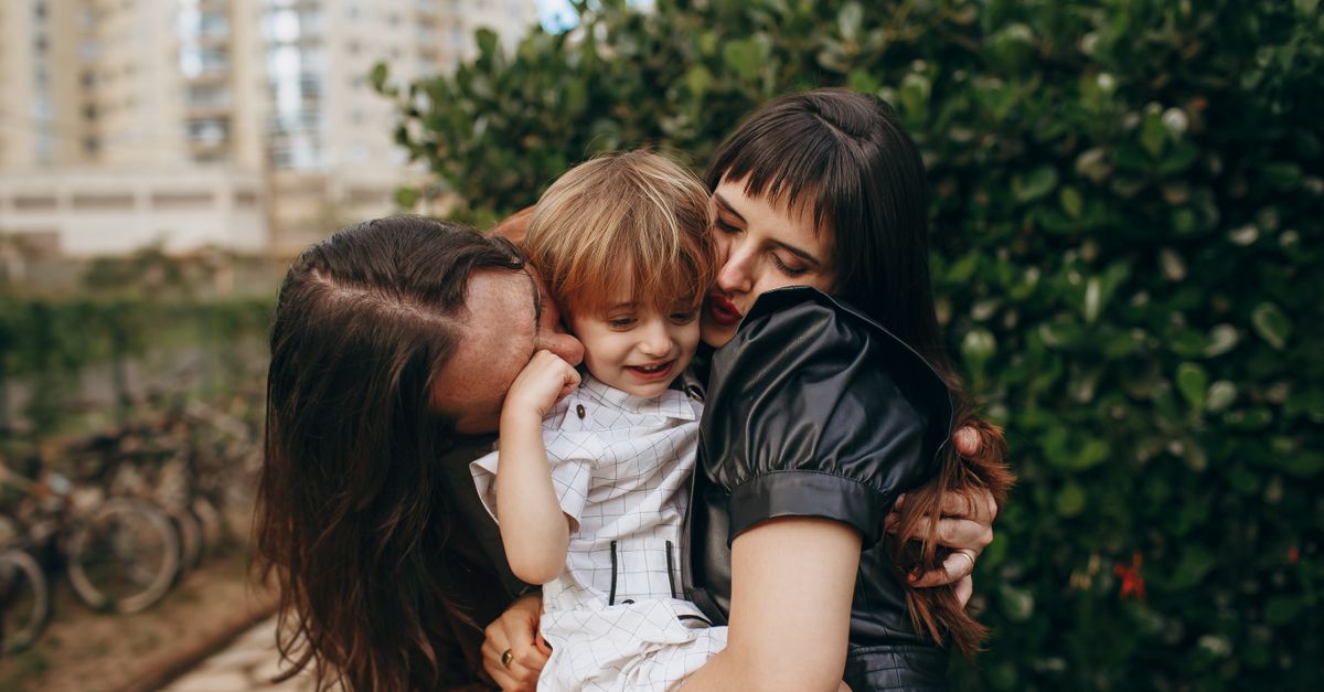 A joyful family moment captured outdoors with two adults hugging a child.