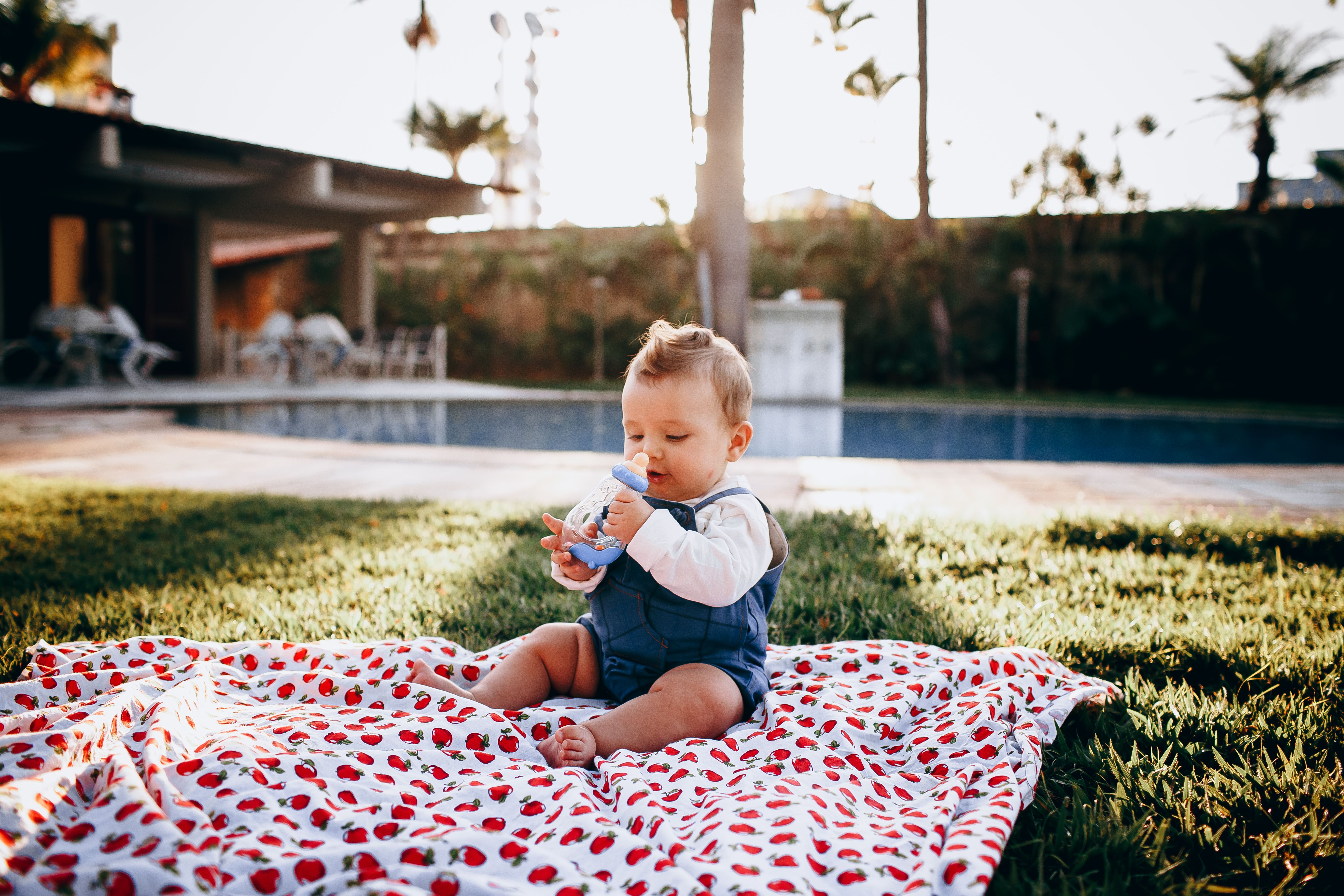 An adorable baby enjoying time outdoors on a patterned blanket in a backyard setting.