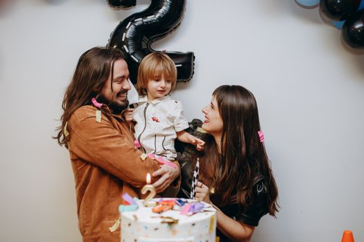 Happy family with child celebrating second birthday with cake and decorations indoors.