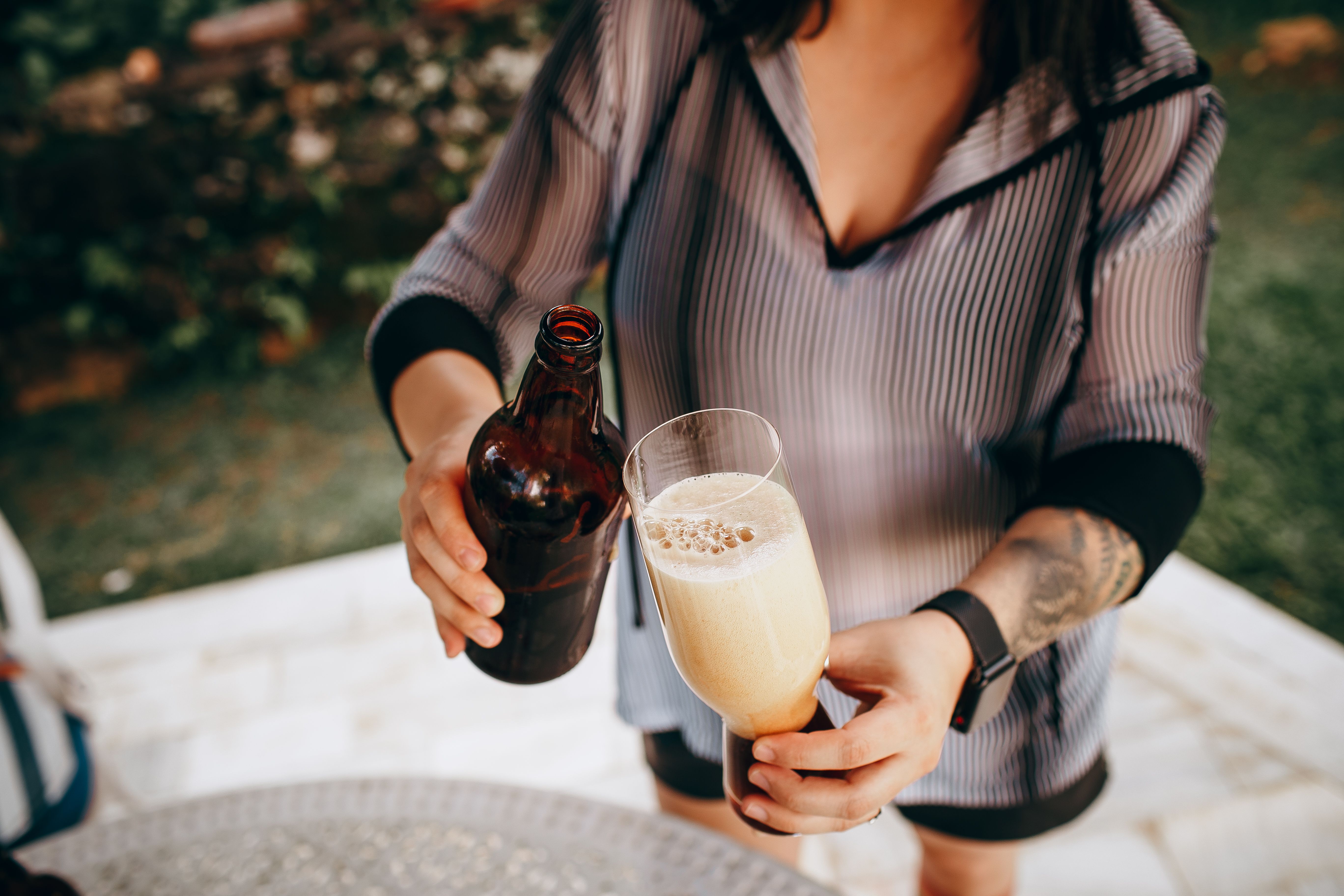 Close-up of a woman pouring beer from a brown bottle into a glass outdoors.