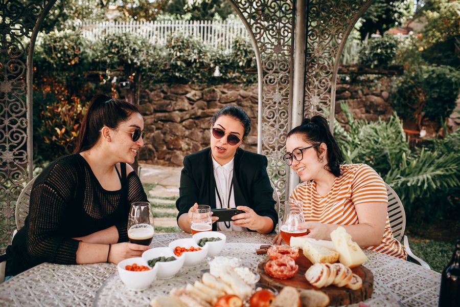 Three hosts talking over a garden table set with cheese, bread and cider, photo by Helena Lopes