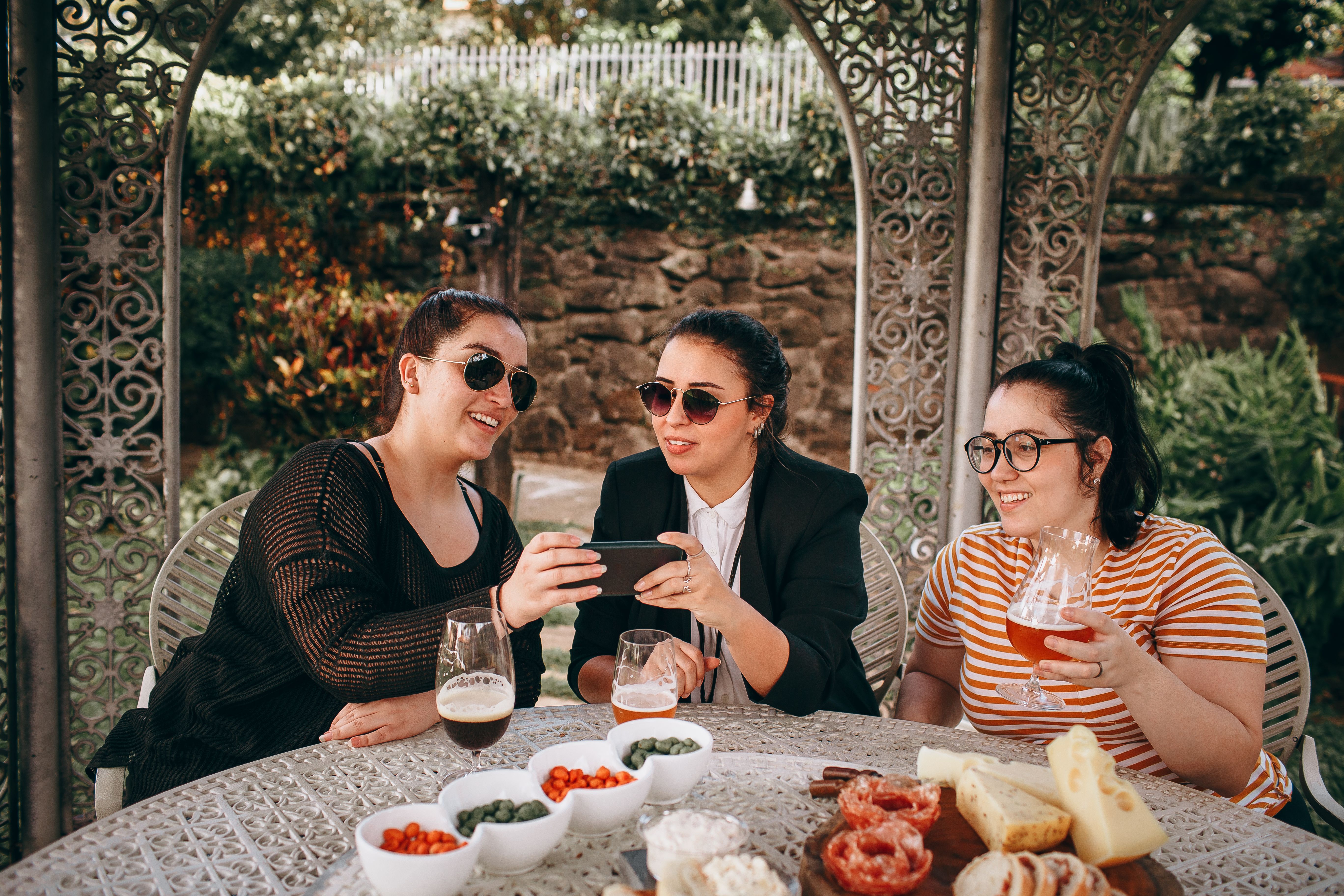 Three friends enjoy a relaxed outdoor gathering with drinks, laughter, and snacks.