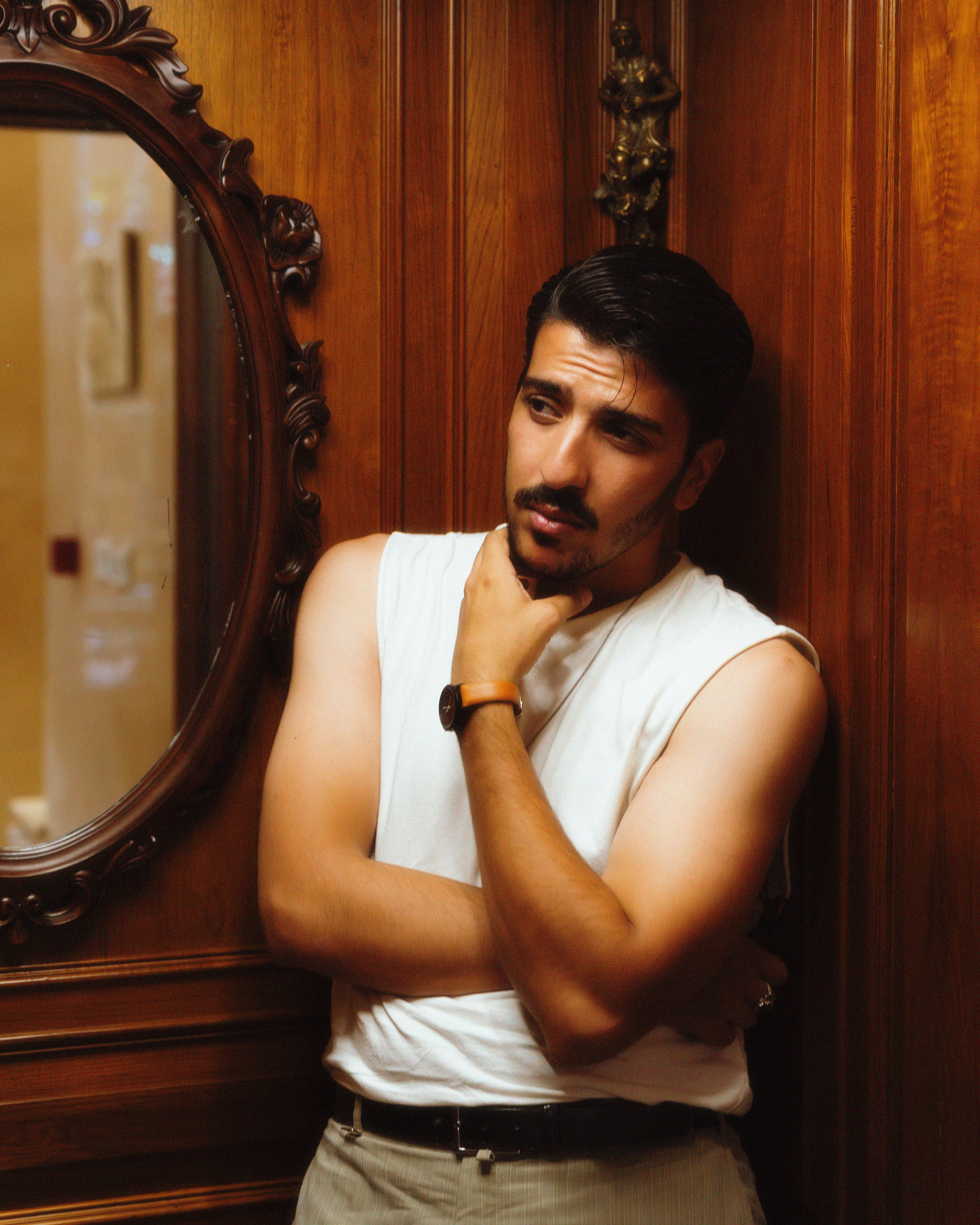 A stylish man poses thoughtfully against a vintage wooden wall, reflecting elegance.