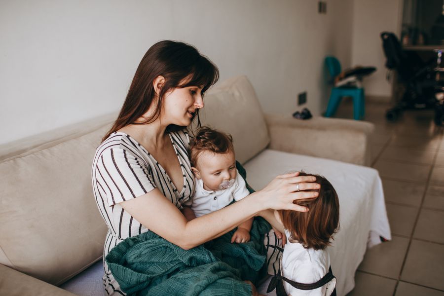 Mãe cuidando carinhosamente dos dois filhos em casa, em um momento de acolhimento familiar
