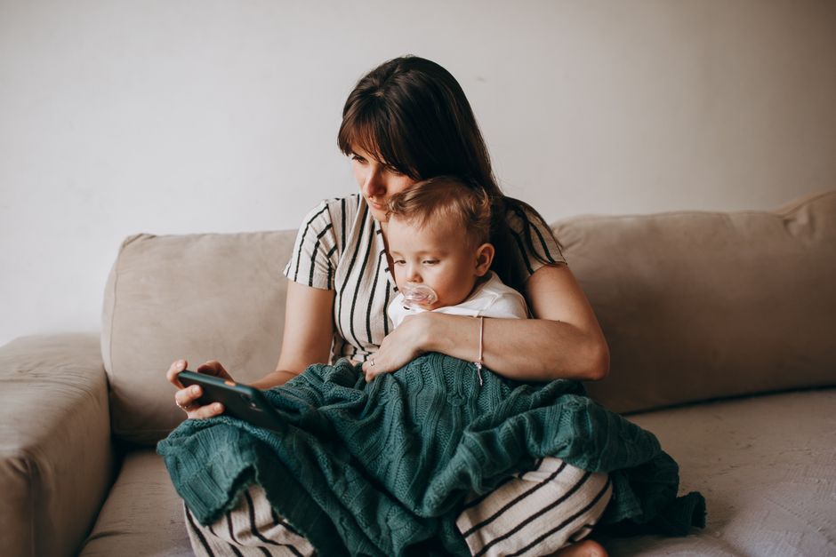 A mother and baby relaxing together on a cozy sofa indoors, sharing a warm family moment.
