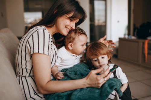Free Happy mother engaging with her two young sons at home using a smartphone. Stock Photo