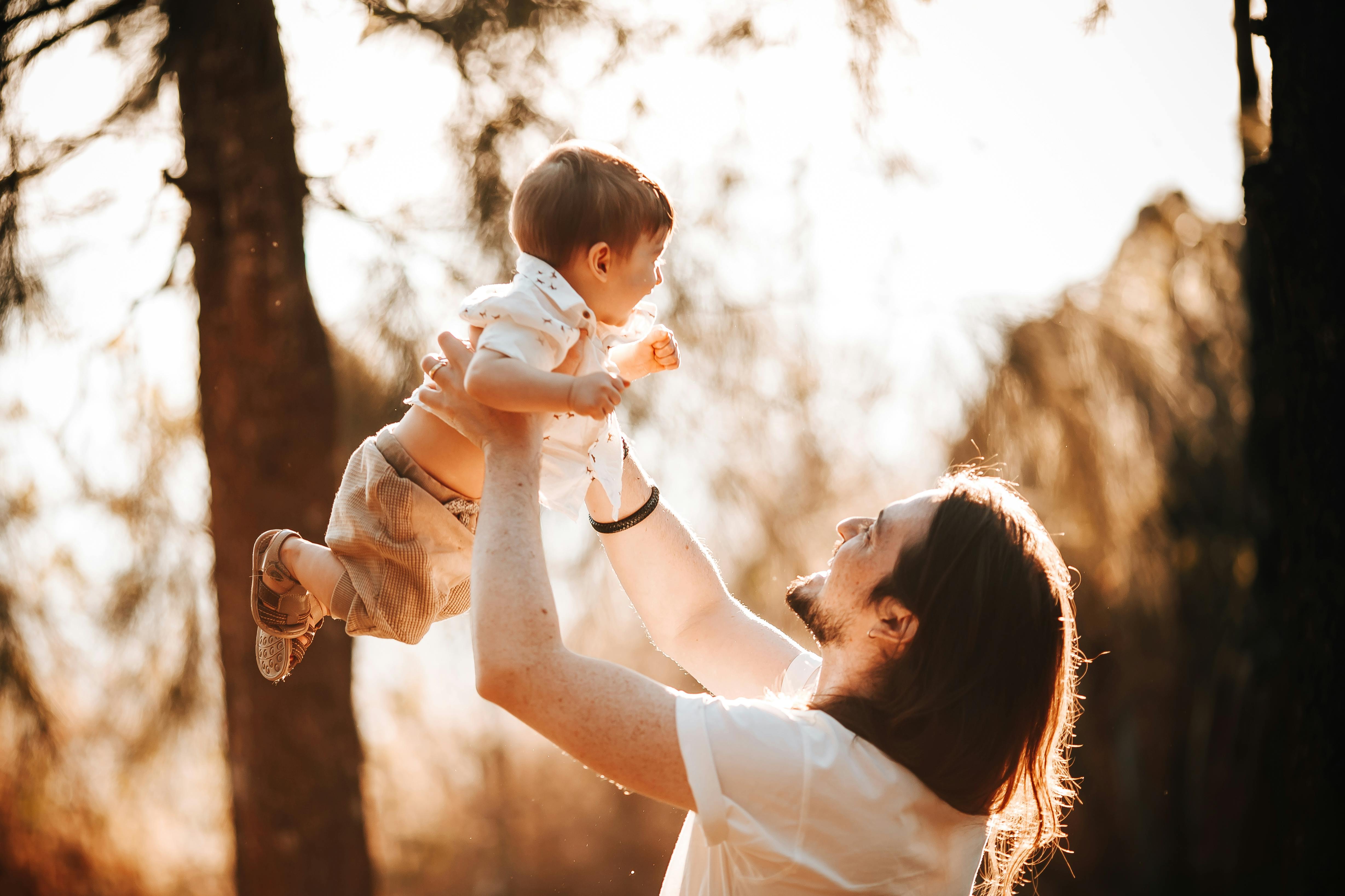 A man holding his son in the air in the woods