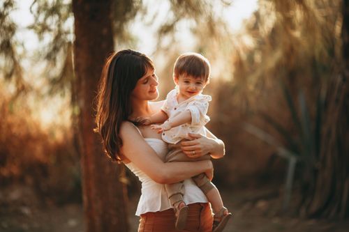 Free A mother lovingly embraces her child in a sunlit forest, capturing a moment of joy and togetherness. Stock Photo