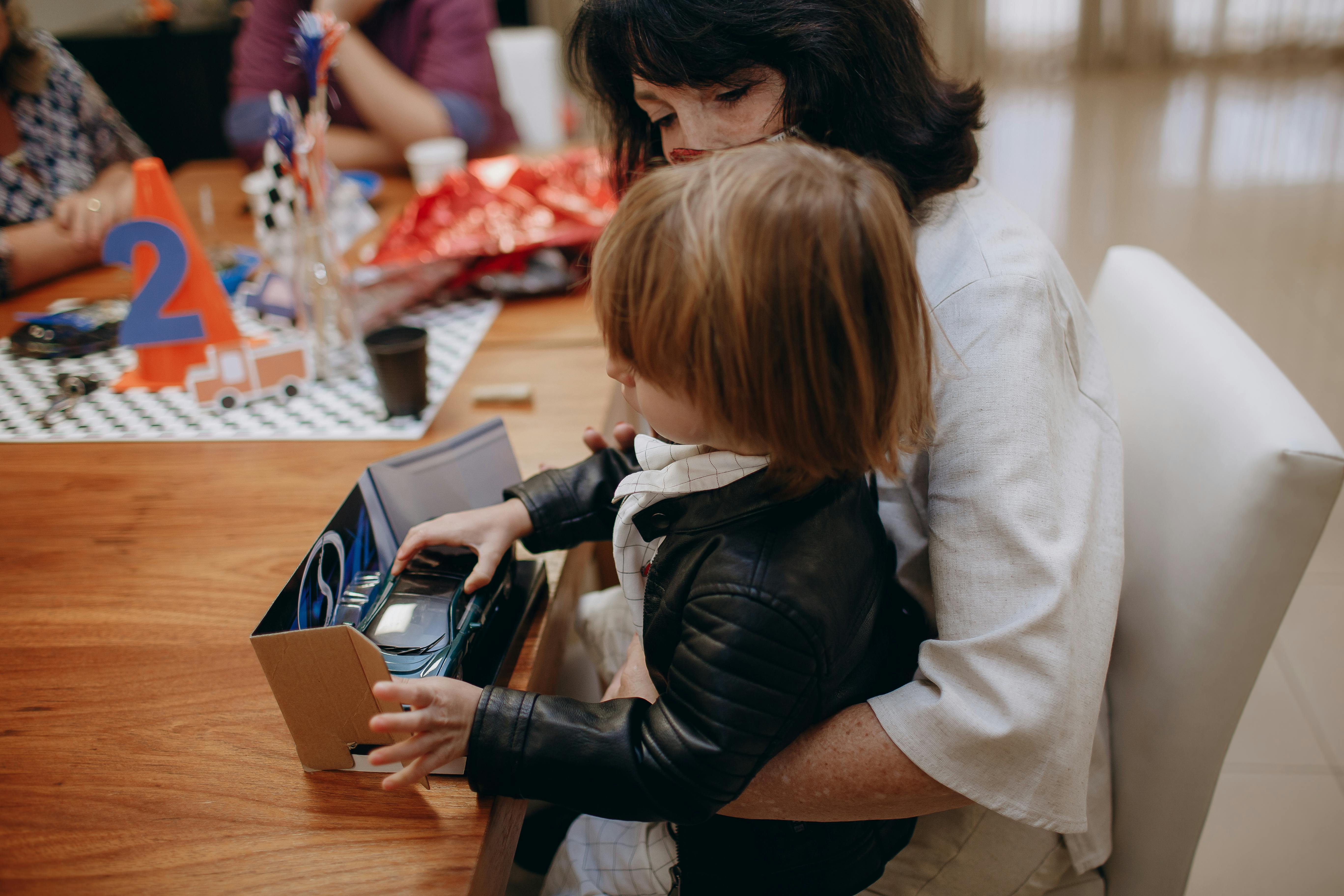 A mother and child opening a gift during a birthday party, featuring a toy car.