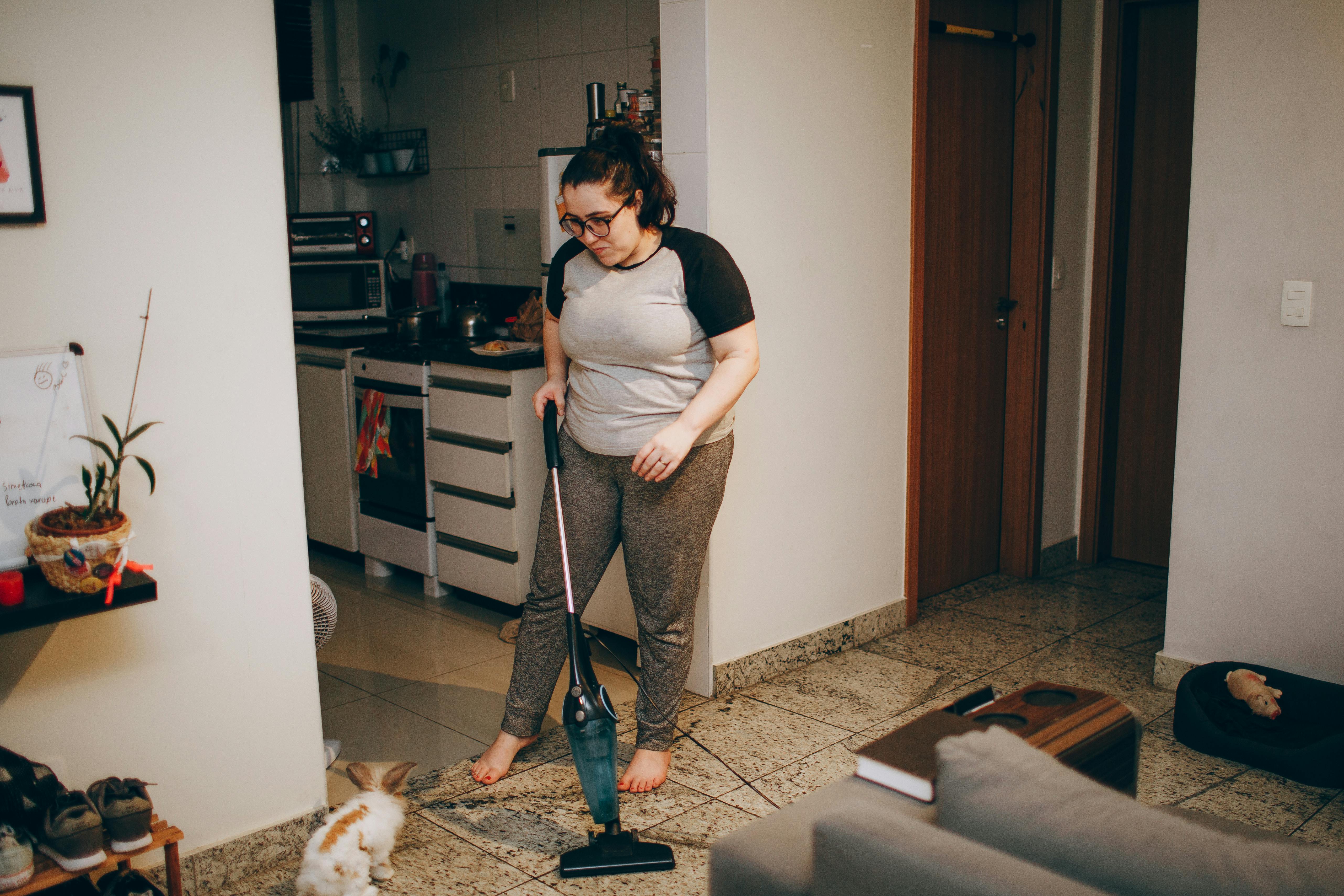 tips for managing pet allergies at home - A woman cleaning her living room with a vacuum cleaner while her pet rabbit watches.