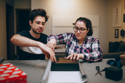 Free A man and woman wrapping a gift together indoors, showcasing teamwork and creativity. Stock Photo