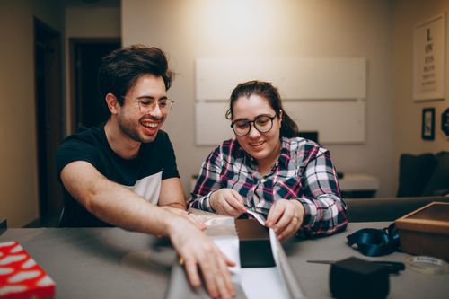 Free Smiling couple wrapping gifts together indoors, enjoying creative time at home. Stock Photo