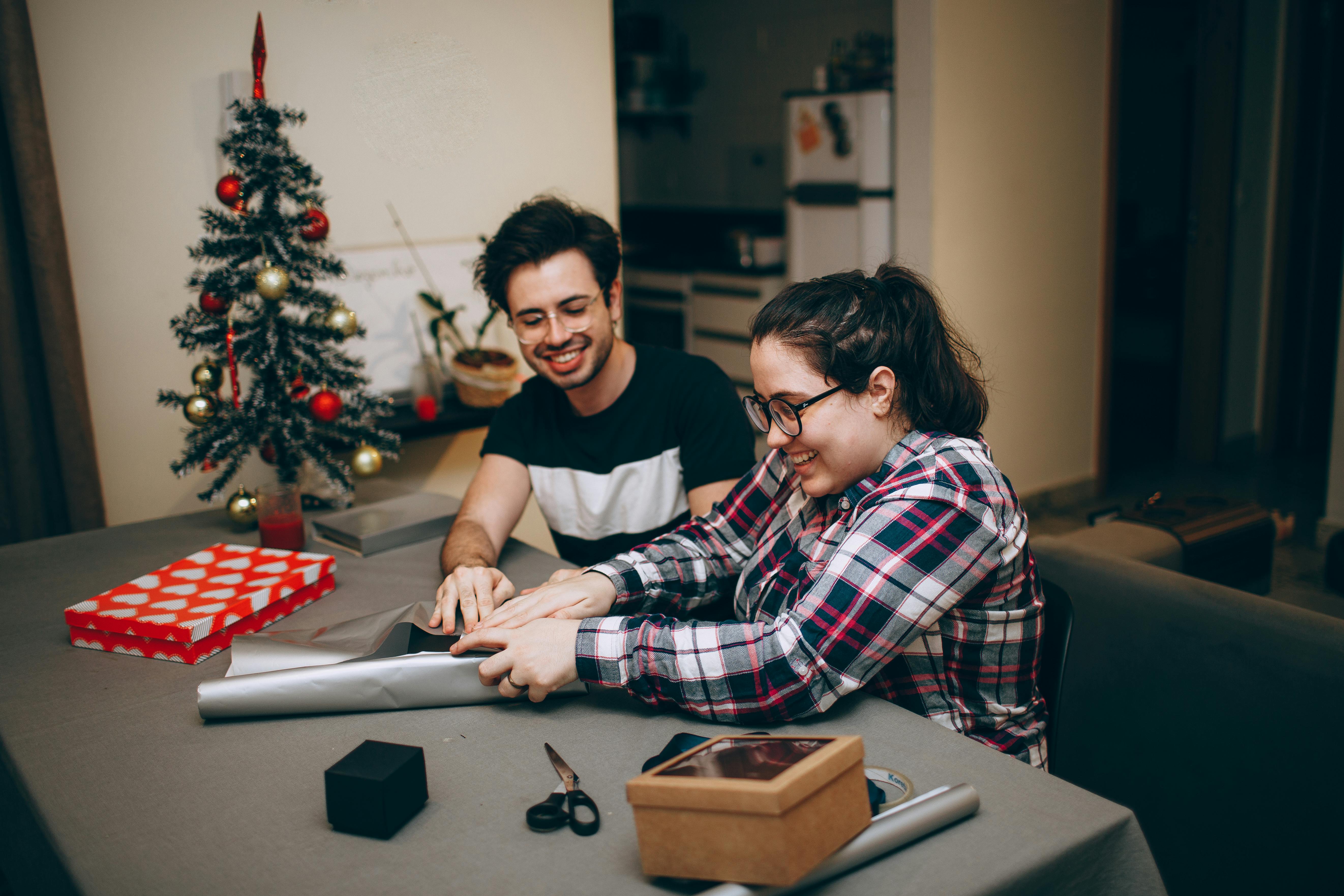 Couple wrapping gifts for Christmas at home, enjoying festive holiday atmosphere.