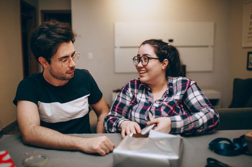 Free Man and woman happily wrapping a gift inside a cozy room, fostering togetherness. Stock Photo