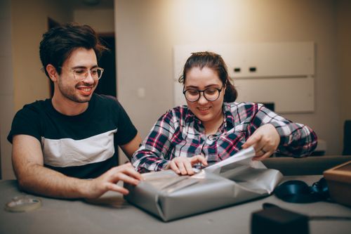Free Smiling couple unwrapping a present indoors, enjoying a moment of togetherness. Stock Photo