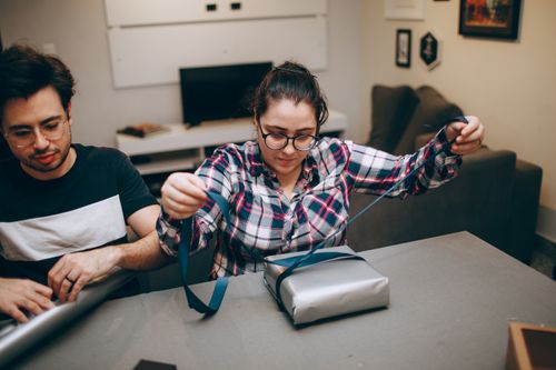 Free Two young adults wrapping gifts in a cozy indoor setting with concentration and creativity. Stock Photo