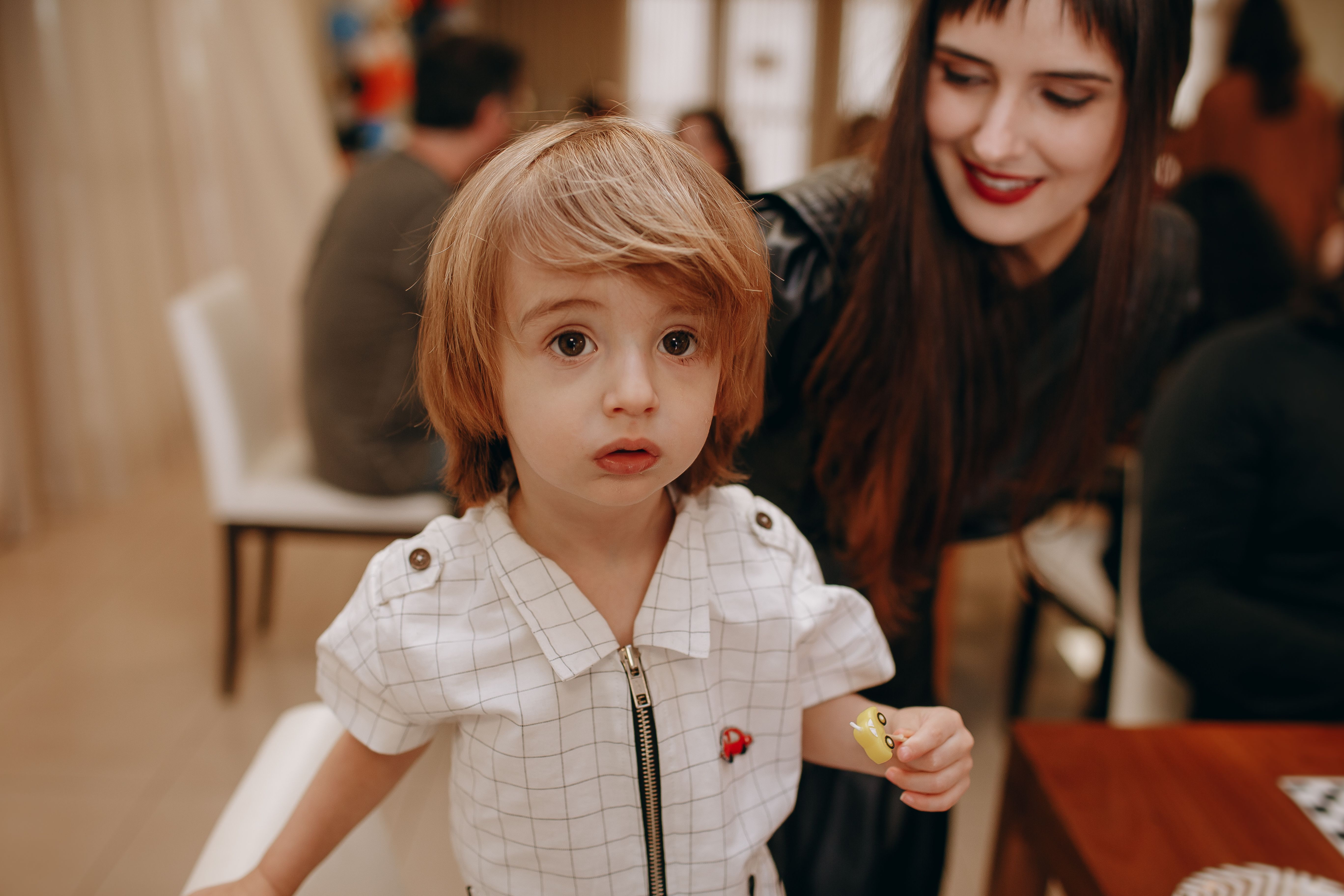 A heartwarming indoor scene capturing the innocent curiosity of a child with a motherly figure nearby.