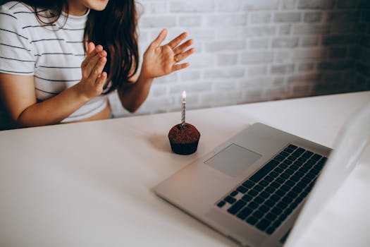 Woman clapping near a cupcake with candle on a virtual birthday setup.