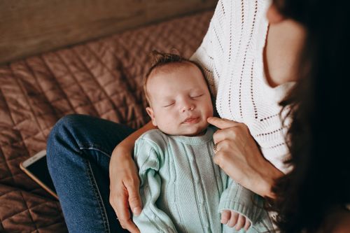 Free A serene photograph of a mother cradling her sleeping baby indoors, capturing warmth and love. Stock Photo