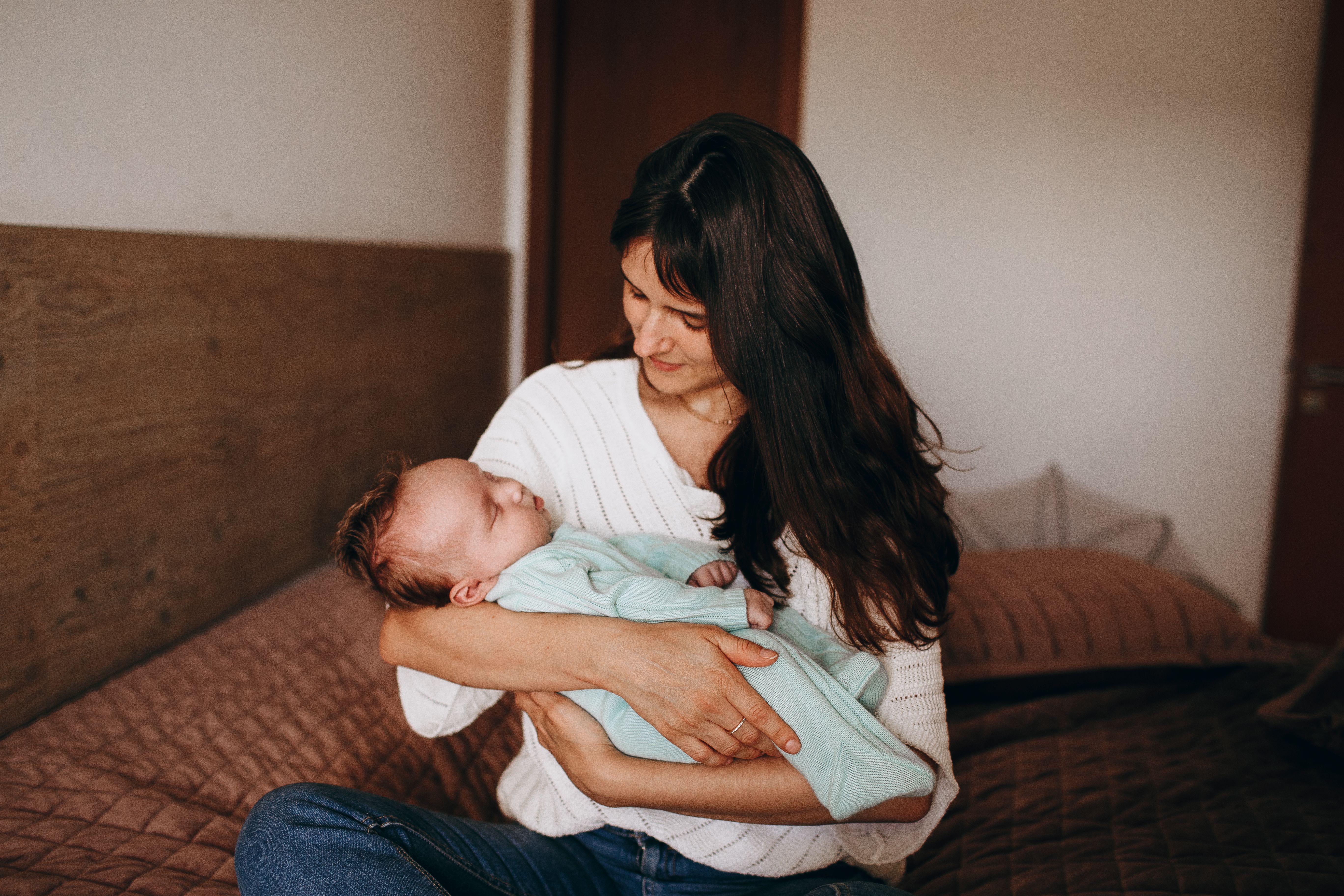 A mother lovingly cradles her sleeping baby in a comfortable bedroom, radiating warmth and affection.